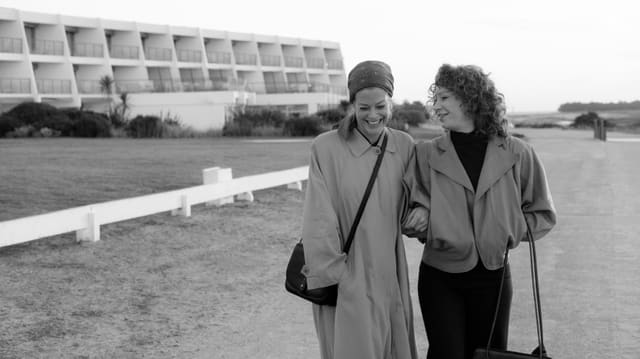 Zei Frauen spazieren am Strand, links ein Häuserkomplex. Die beiden lächeln. Zei Frauen spazieren am Strand, links ein Häuserkomplex. Die beiden lächeln.