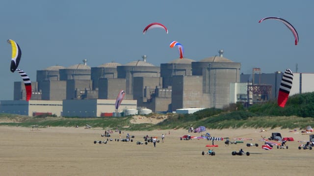 Sechs grosse Betonreaktoren stehen hinter einem Strand, auf dem Personen Drachen steigen lassen. Sechs grosse Betonreaktoren stehen hinter einem Strand, auf dem Personen Drachen steigen lassen.