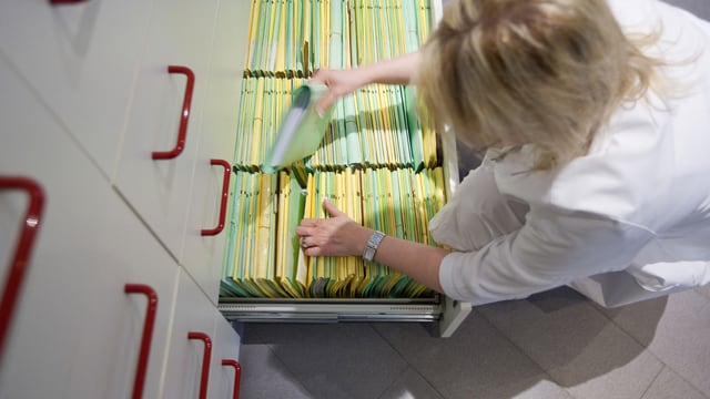 Eine Arzthelferin räumt eine Patientenakte zurück in eine Schublade. Eine Arzthelferin räumt eine Patientenakte zurück in eine Schublade.