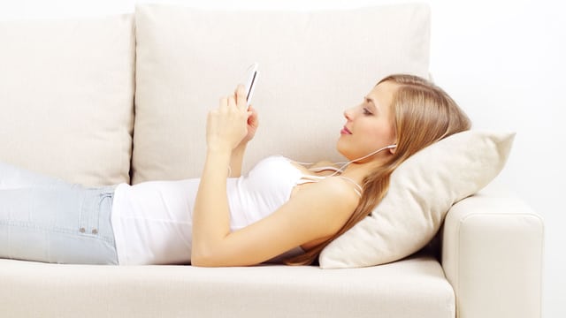 Eine junge Frau liegt auf dem Sofa und hält ein Handy in der Hand. Eine junge Frau liegt auf dem Sofa und hält ein Handy in der Hand.