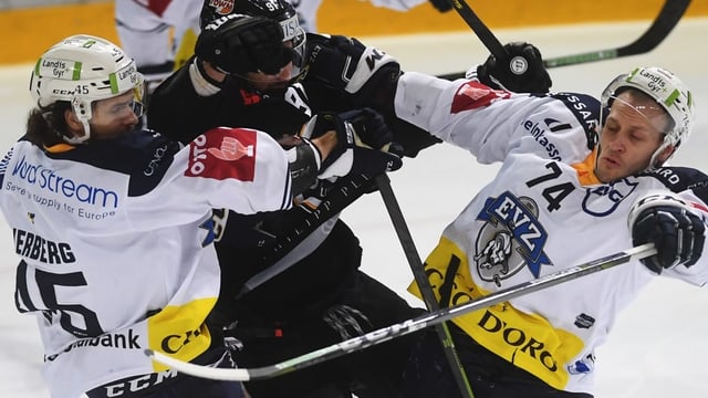 Zwei Spieler des EV Zug nehmen einen Spieler von Lugano in die Mangel. Zwei Spieler des EV Zug nehmen einen Spieler von Lugano in die Mangel.