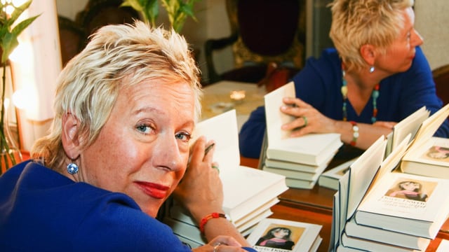Eine Frau mit kurzen Haaren sitzt an einem Tisch voller Bücher. Eine Frau mit kurzen Haaren sitzt an einem Tisch voller Bücher.