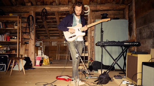 Labrador City-Sänger Nik Stettler in einer Alphütte am Gitarre spielen.