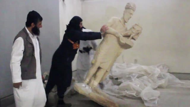 Von Kopf bis Fuss schwarz eingehüllter Mann stösst lebensgrosse weisse Statue um. Von Kopf bis Fuss schwarz eingehüllter Mann stösst lebensgrosse weisse Statue um.