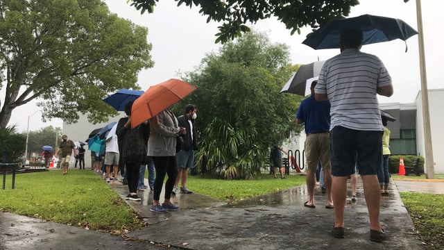 Menschen stehen Schlange mit Regenschirmen Menschen stehen Schlange mit Regenschirmen