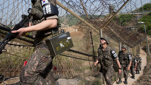 Soldaten laufen einen Stacheldrahtzaun entlang. Soldaten laufen einen Stacheldrahtzaun entlang.
