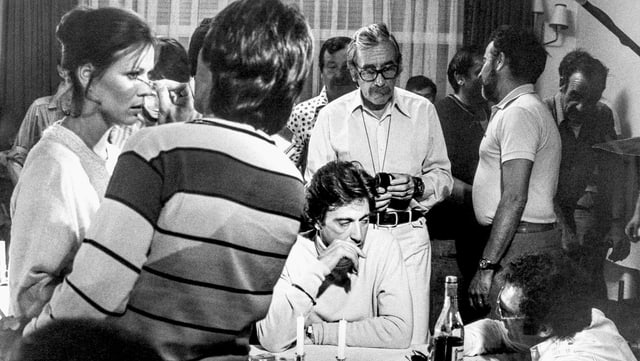 Filmset: Viele Personen in einem Raum, eine wird geschinkt, zwei sitzen an einem Tisch. Filmset: Viele Personen in einem Raum, eine wird geschinkt, zwei sitzen an einem Tisch.