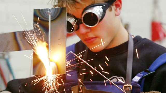 Junger Mann mit dicker Schutzbrille schweisst ein Stück Metall, Funken sprühen. Junger Mann mit dicker Schutzbrille schweisst ein Stück Metall, Funken sprühen.