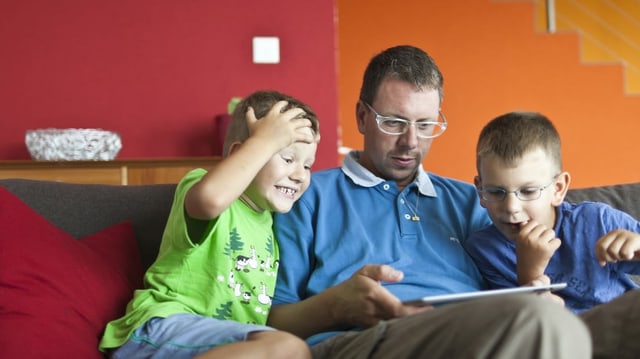 Vater sitzt mit seinen Söhnen auf dem Sofa und schauf auf ein Tablet Vater sitzt mit seinen Söhnen auf dem Sofa und schauf auf ein Tablet