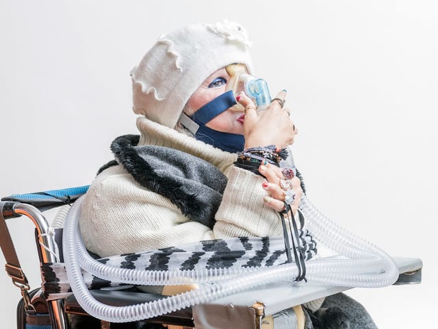 Eine ältere Frau atmet durch eine Maske, an die ein Schlauch angeschlossen ist. Eine ältere Frau atmet durch eine Maske, an die ein Schlauch angeschlossen ist.