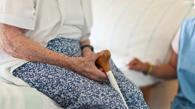 Eine alte Frau sitzt auf einem Bettrand. Eine alte Frau sitzt auf einem Bettrand.