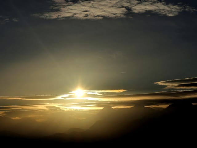 Sonne hinter Wolken über Bergpanorama