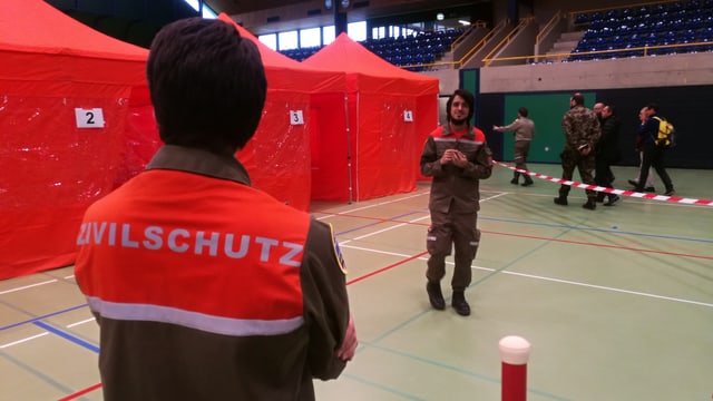 Mann mit Zivilschutz-Jacke vor Zelten Mann mit Zivilschutz-Jacke vor Zelten
