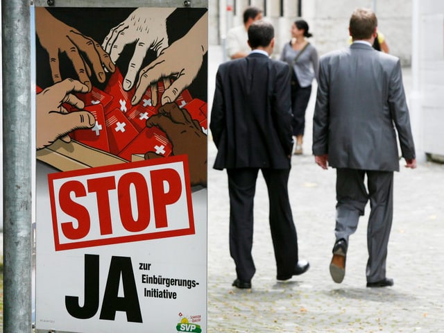 Wahlplakat, darauf: Viele Hände greifen nach Schweizerpässen. Neben Plakat laufen zwei Männer vorbei. Wahlplakat, darauf: Viele Hände greifen nach Schweizerpässen. Neben Plakat laufen zwei Männer vorbei.