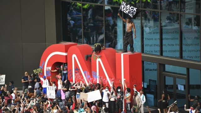 Demonstranten vor einem grossen CNN-Logo, schwenken Flaggen Demonstranten vor einem grossen CNN-Logo, schwenken Flaggen