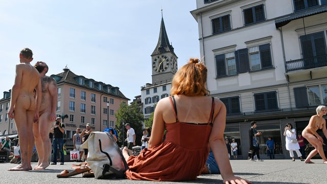 Angezogene Frau sitzt am Boden und betrachtet zwei nackte Männer. Angezogene Frau sitzt am Boden und betrachtet zwei nackte Männer.