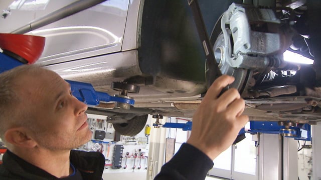 Mann schaut unter ein Auto Mann schaut unter ein Auto