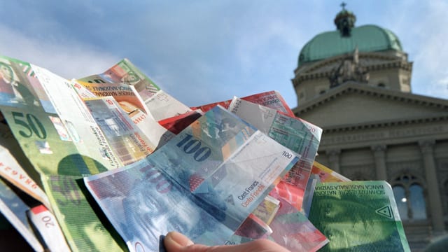 Eine Person hält einen Bündel Geld vor dem Bundeshaus. Eine Person hält einen Bündel Geld vor dem Bundeshaus.