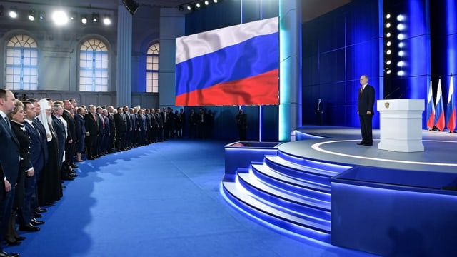 Putin steht auf Bühne, vor ihm Publikum. Putin steht auf Bühne, vor ihm Publikum.