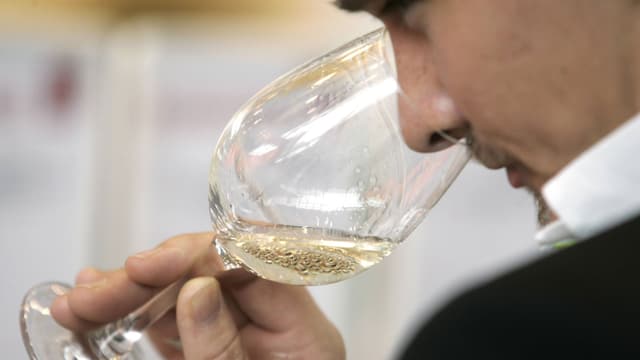 Ein Mann riecht an einem Glas mit Weisswein. 