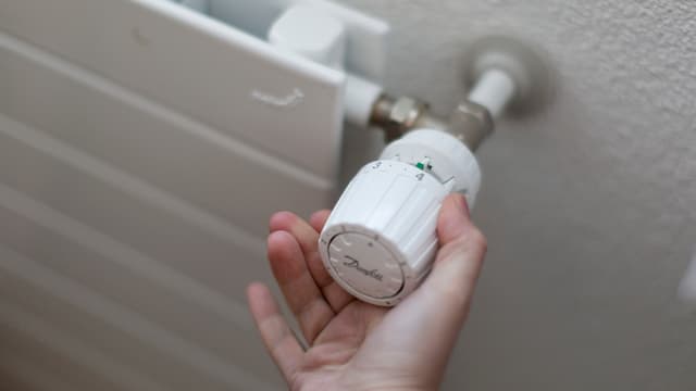Eine Hand dreht den Thermostat an einem Heizkörper. Eine Hand dreht den Thermostat an einem Heizkörper.