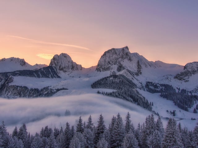 Nebel vor Bergkette, Himmel in rötlichen Farbtönen.