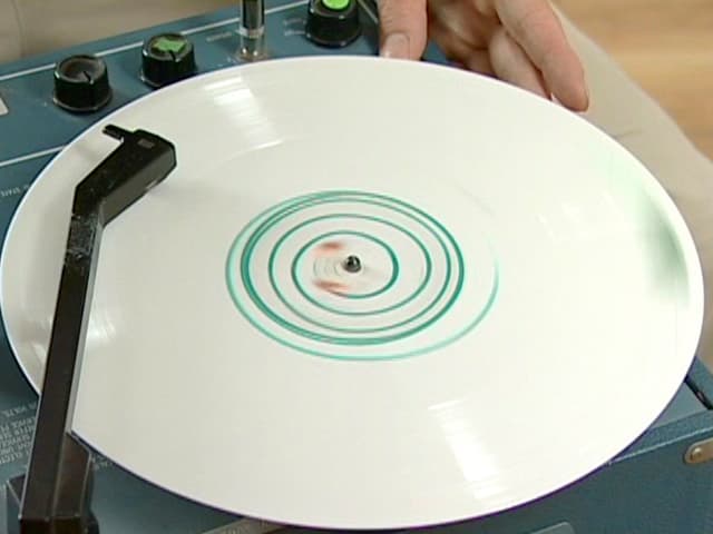 Eine weisse Platte mit grünen Zeichnungen liegt auf einem Plattenspieler. Eine weisse Platte mit grünen Zeichnungen liegt auf einem Plattenspieler.