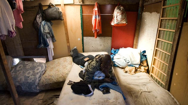 Ein afrikanischer Mann auf einer Matratze in einer baufälligen Hütte Ein afrikanischer Mann auf einer Matratze in einer baufälligen Hütte