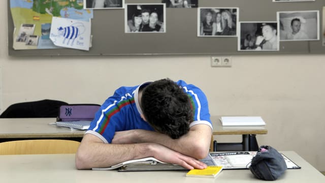 Ein Schüler sitzt schlafend vornüber gebäugt am Pult. Ein Schüler sitzt schlafend vornüber gebäugt am Pult.