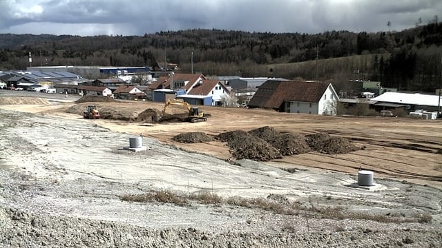 Aufgefüllte Grube, Steine und Erde. Dahinter Wohnhäuser. Aufgefüllte Grube, Steine und Erde. Dahinter Wohnhäuser.