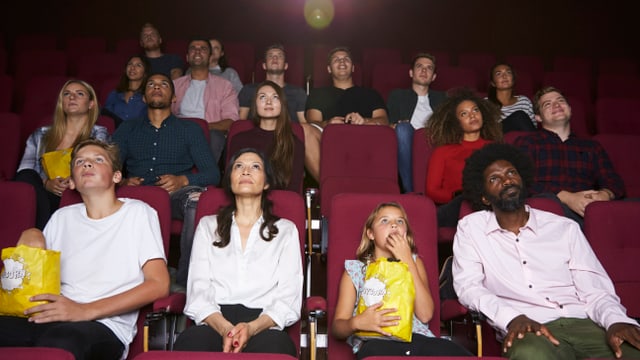 Mehrere Reihen von Männern, Frauen und Kindern schauen Kino und essen Popcorn Mehrere Reihen von Männern, Frauen und Kindern schauen Kino und essen Popcorn