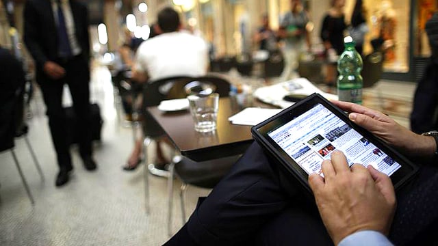 Blick in ein Strassencafé. Ein Mann hält ein Computer-Tablet auf den Knien.