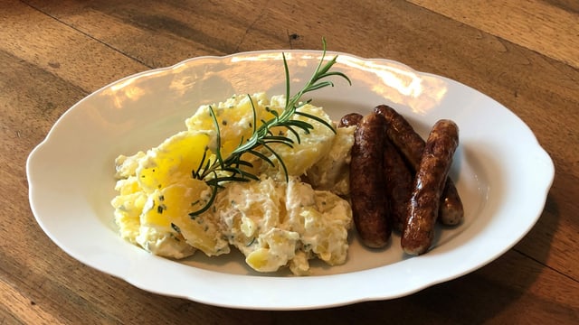 Ein Teller mit Kartoffelsalat und gebratenen Würsten.Garniert mit einem Rosmarinzweig. Ein Teller mit Kartoffelsalat und gebratenen Würsten.Garniert mit einem Rosmarinzweig.
