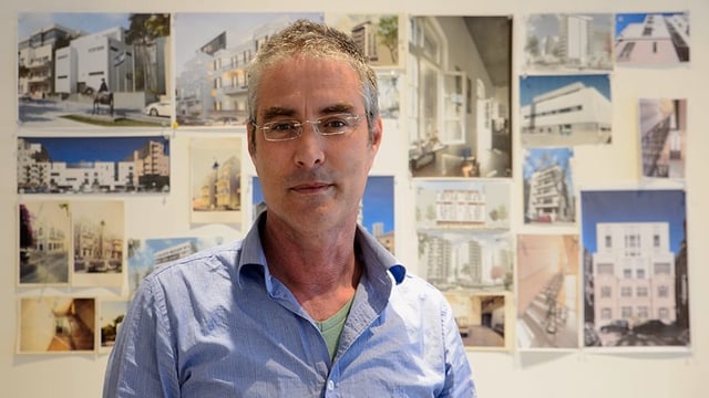 Ein mann mit hellblauem Hemd, hinter ihm an der Wand hängen Fotos von Gebäuden. Ein mann mit hellblauem Hemd, hinter ihm an der Wand hängen Fotos von Gebäuden.