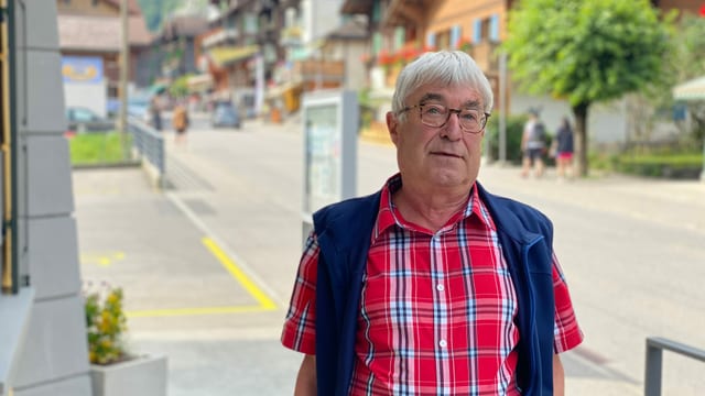 Mann steht in rot-blau-kariertem Hemd an einer Dorfstrasse Mann steht in rot-blau-kariertem Hemd an einer Dorfstrasse