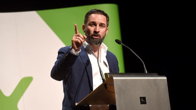 Der schwarzhaarige und baarttragende Abascal bei einer Rede am Rednerpult. Hinter ihm ein Plakat mit grünem Vox-Logo. Der schwarzhaarige und baarttragende Abascal bei einer Rede am Rednerpult. Hinter ihm ein Plakat mit grünem Vox-Logo.