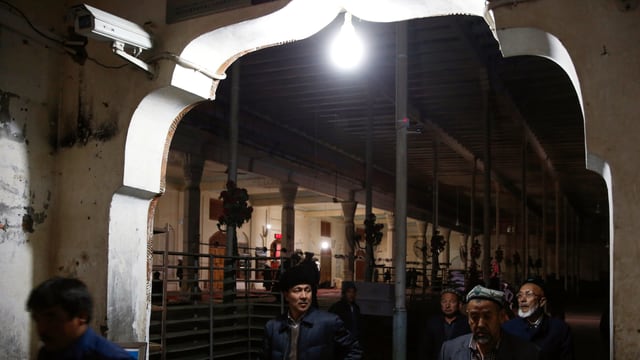 Mitglieder der uigurischen Minderheit in China laufen nach dem Verlassen einer Moschee an einer Überwachungskamera vorbei. Mitglieder der uigurischen Minderheit in China laufen nach dem Verlassen einer Moschee an einer Überwachungskamera vorbei.
