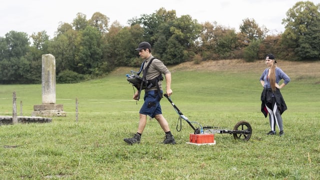 Forscher läuft mit Bildschirm um den Hals und Radargerät an Handwagen über Wiese Forscher läuft mit Bildschirm um den Hals und Radargerät an Handwagen über Wiese