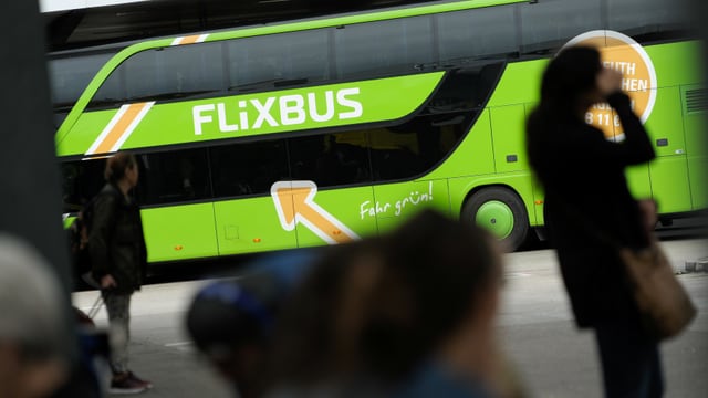 Ein Flixbus an einem Busbahnhof. Im Vordergrund sind Passagiere.