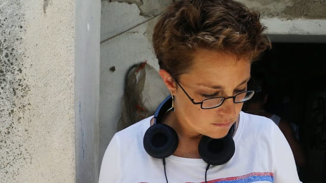 Die Grossaufnahme einer Frau mit Brille und kurzen Haaren. Sie schaut zu Boden. Um den Hals hat sie einen Kopfhörer. Die Grossaufnahme einer Frau mit Brille und kurzen Haaren. Sie schaut zu Boden. Um den Hals hat sie einen Kopfhörer.