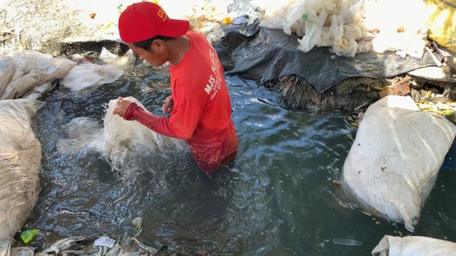 Ein Mann wäscht Plastik in einem aufgestauten, sehr schmutzigen Bach. Ein Mann wäscht Plastik in einem aufgestauten, sehr schmutzigen Bach.