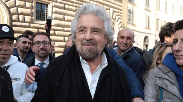Der weisshaarige Grillo umgeben von Männern, er lächelt. Der weisshaarige Grillo umgeben von Männern, er lächelt.