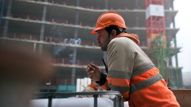Ein Mann raucht auf einer Baustelle. Ein Mann raucht auf einer Baustelle.