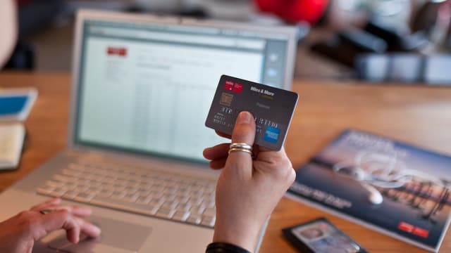 Frau hält Kreditkarte in der Hand, im Hintergrund Computer.