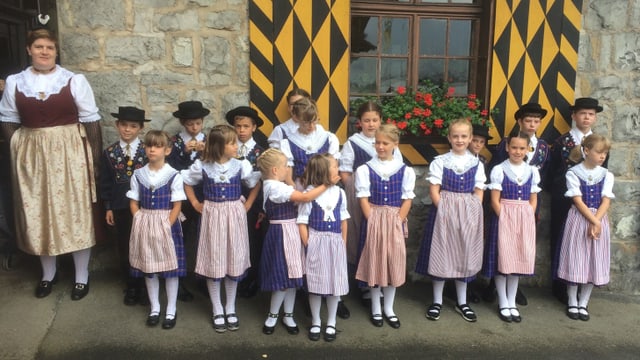 Eine Gruppe von Kindern in Trachten steht vor einem Steinhaus. Eine Gruppe von Kindern in Trachten steht vor einem Steinhaus.