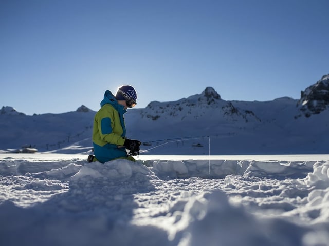 Ein Junge kniet auf einem gefrorenen See und hält eine Angel in ein Eisloch. Ein Junge kniet auf einem gefrorenen See und hält eine Angel in ein Eisloch.