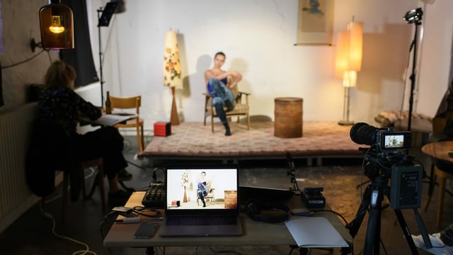 Eine Frau sitzt auf einer improvisierten Bühne und wird von einer Kamera gefilmt. Eine Frau sitzt auf einer improvisierten Bühne und wird von einer Kamera gefilmt.