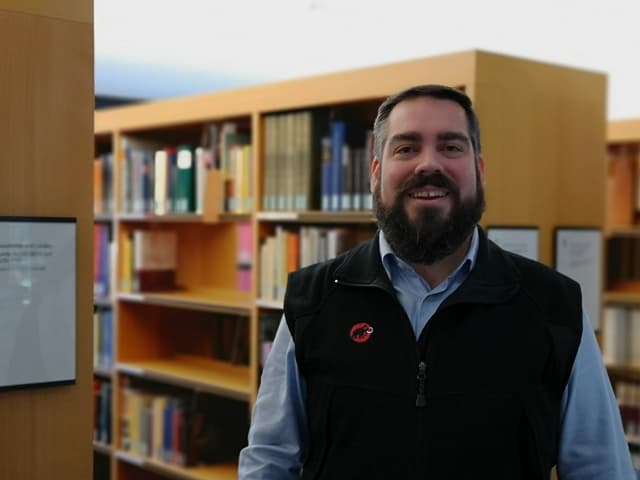 Mann mit Bart vor Bücherregal. Mann mit Bart vor Bücherregal.