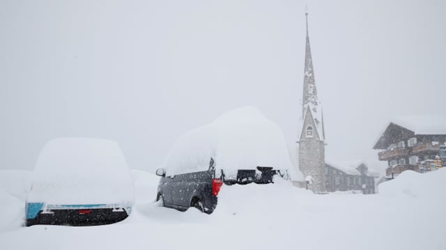 Von Schnee zugedeckte Autos, im Hintergrund eine Kirche im Schneefall. Von Schnee zugedeckte Autos, im Hintergrund eine Kirche im Schneefall.