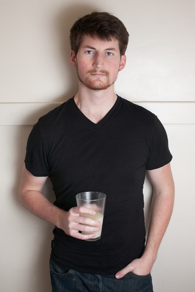Ein Mann im Schwarzen T-Shirt und einem Glas in der Hand blickt ernst in die Kamera.